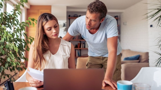 a husband and wife looking at documents and a laptop.