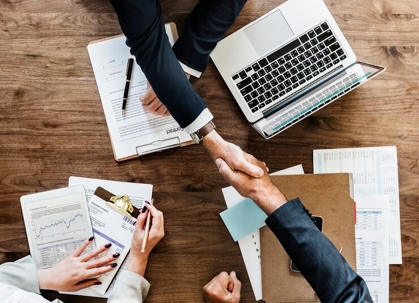 two people shaking hands over a desk.